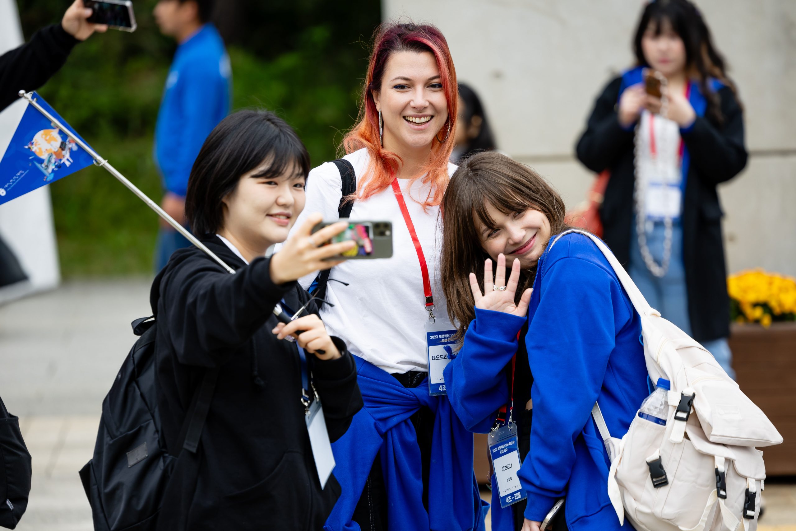 Três mulheres jovens tinham uma selfie. Uma delas segura a bandeira da Coreia.